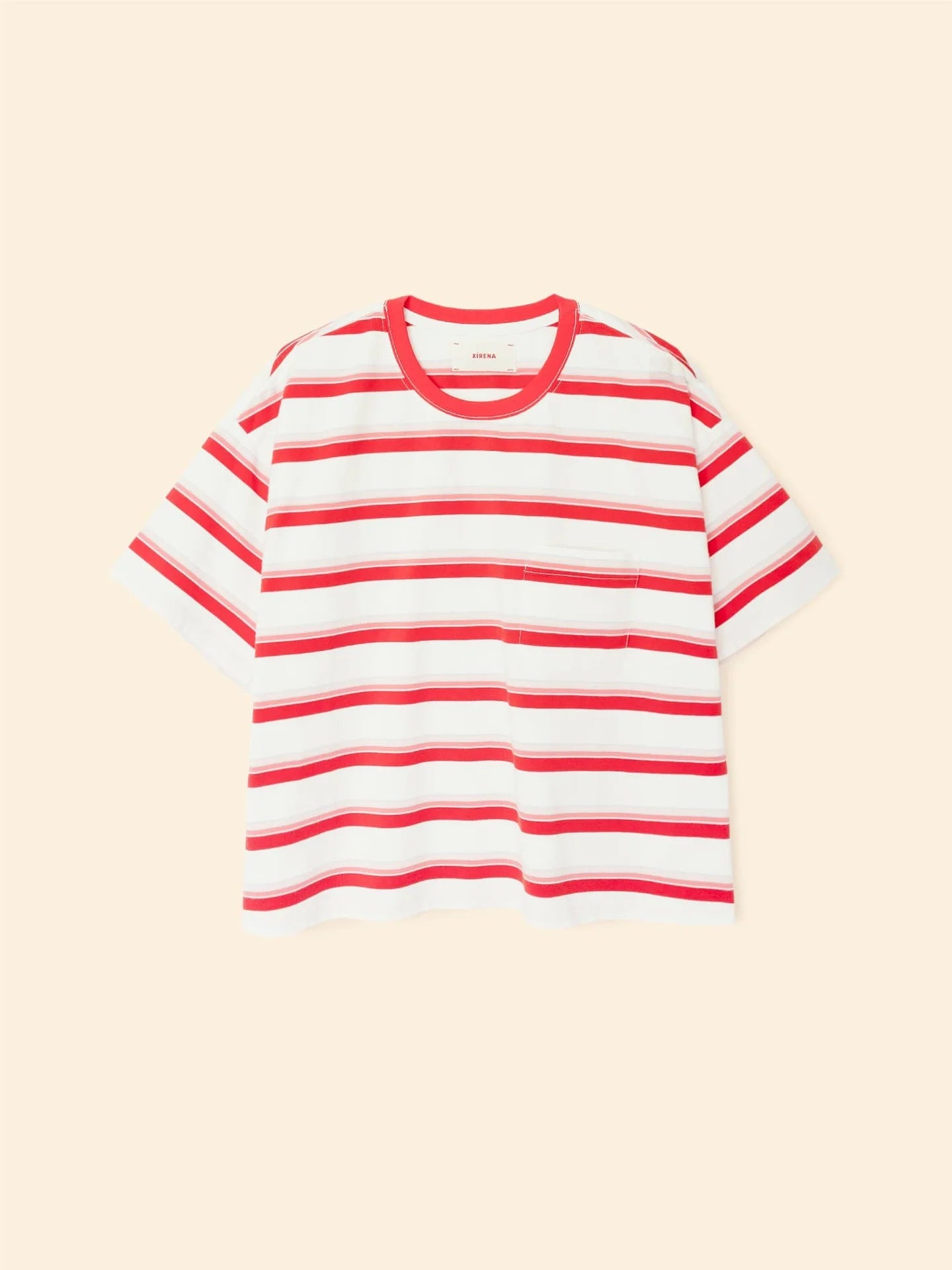 The Xirena Paulina Tee is a short-sleeved striped cotton jersey shirt with a contrast ringer neck, red horizontal stripes, and a small chest pocket, shown against a light beige background.