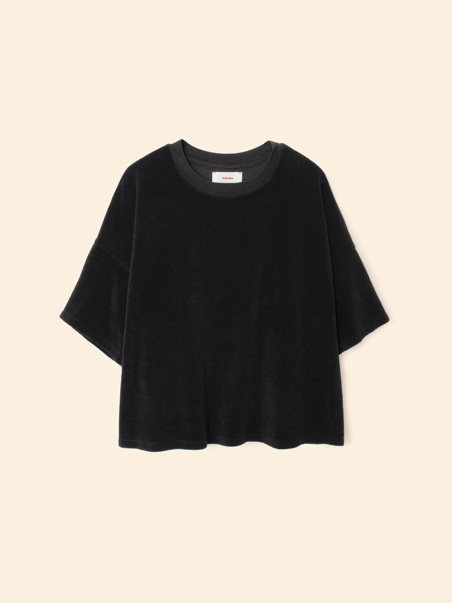 The Roe Top by Xirena is a loose-fitting black short-sleeve t-shirt made from a soft cotton blend with a round neckline, shown on a beige background.