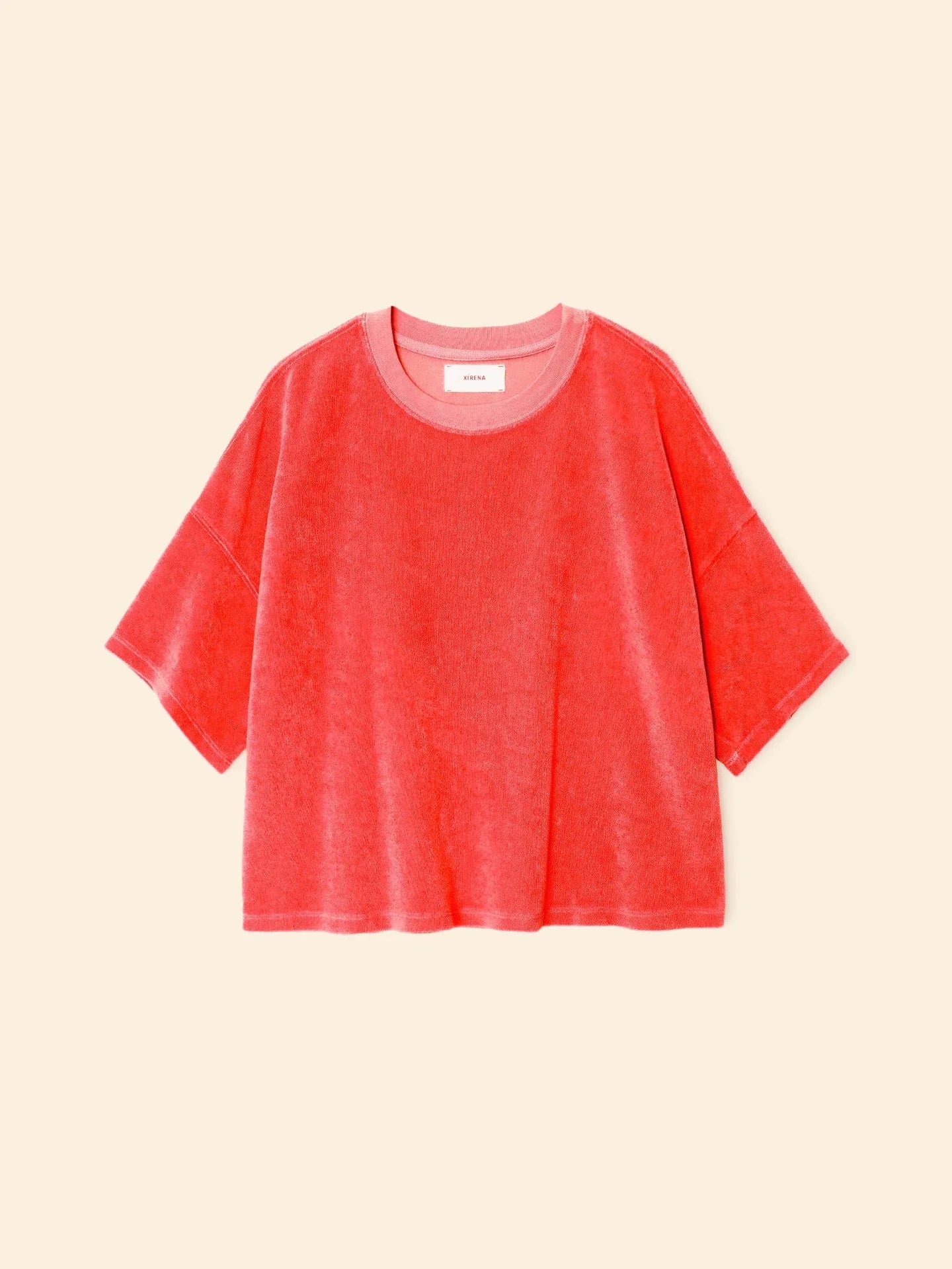 The Roe Top by Xirena is a loose-fitting, short-sleeved T-shirt in bright coral pink, made from a soft cotton blend with a crew neckline, shown against a light beige background.