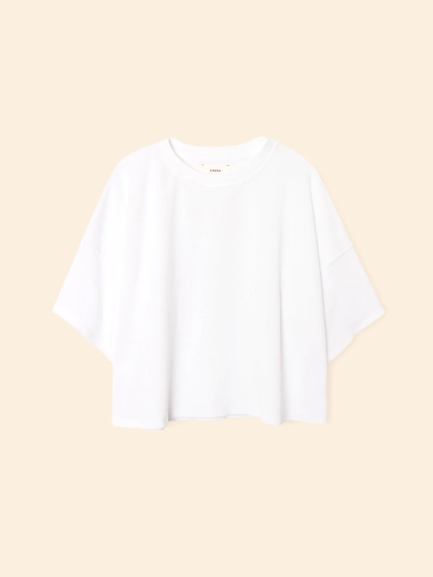 The Roe Top by Xirena is an oversized, short-sleeve T-shirt in plain white, made from a soft cotton blend with a relaxed fit, shown against a beige background.