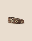 The Francoise Belt by Xirena features brown suede leather, a brass buckle, and gold grommets along its length. Displayed coiled on a light beige background, this adjustable belt adds style to any outfit.