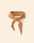 The Xirena Myla Scarf, an ultra-soft light brown cashmere accessory with two pointed ends, is shown tied in a loose knot against a cream backdrop.