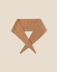 The Xirena Myla Scarf, an ultra-soft cashmere neck scarf in light brown, is laid flat on a cream background with its ends crossed loosely in a V shape at the bottom.