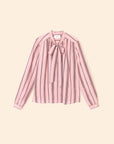 The Sabina Top by Xirena is a long-sleeved blouse with pink, black, and white vertical stripes, made from drapey viscose and finished with a chic bow tie neck, shown against a light beige background.