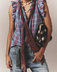 Person wearing a sleeveless, ruffled blue and pink plaid top, maroon scarf, Xirena Stevie Belt, light blue jeans, shell necklace, and carrying a black-and-white checkered bag.