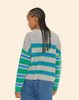 A person with braided hair is seen from the back, wearing a Lela Sweater by Xirena, a gray cashmere garment with blue and green stripes, accompanied by blue jeans. The background is a plain light beige color.
