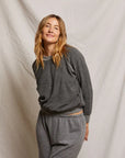 Wearing the Perfectwhitetee Ziggy Reverse LS Sweatshirt, a person with long, wavy blonde hair stands before an off-white fabric backdrop, smiling softly at the camera.