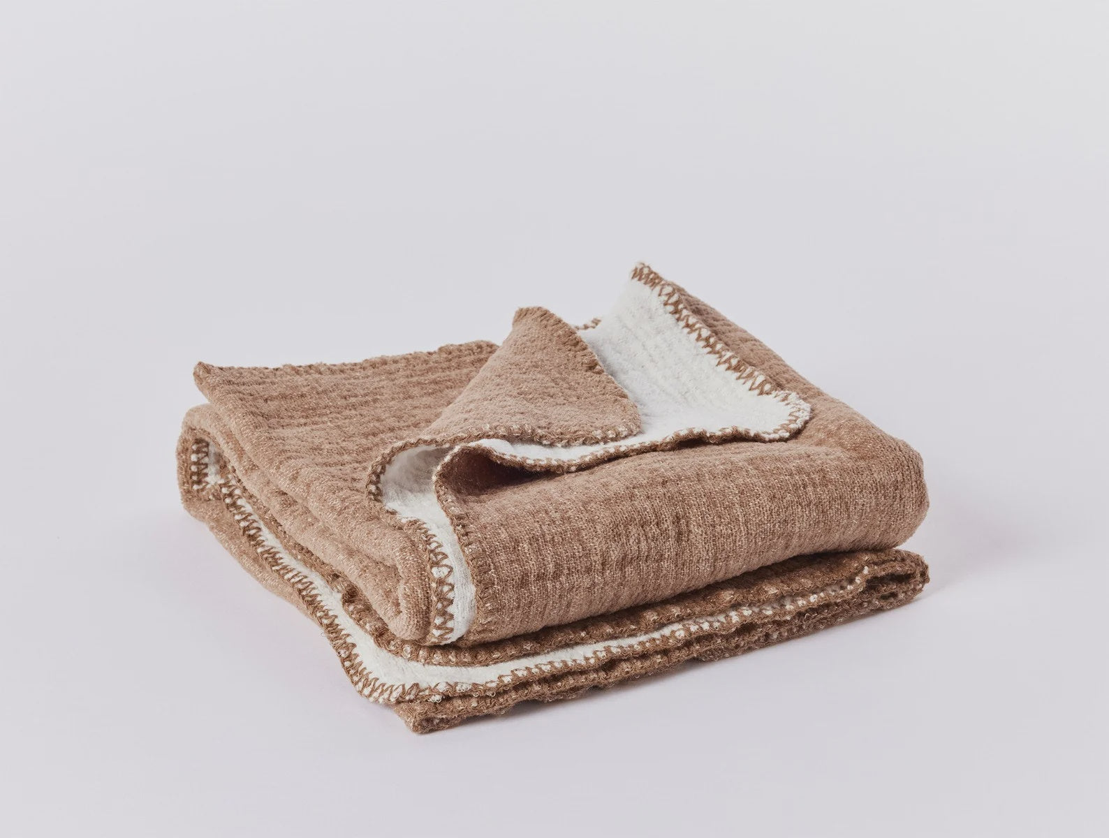 A neatly folded Cozy Cotton Blanket Clay Baby with a white interior and fringed edges, displayed against a plain light background in a Scottsdale Arizona bungalow by Coyuchi Inc.