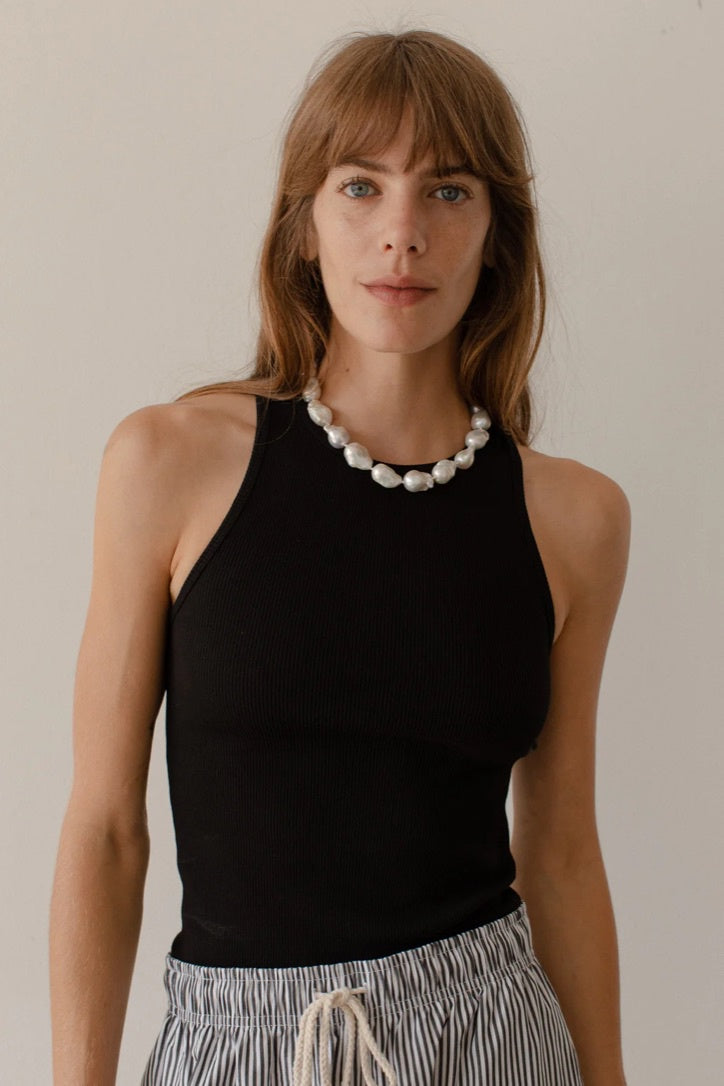A woman with shoulder-length brown hair, wearing a Donni black sleeveless Rib Tank and a pearl necklace, stands against a neutral background in Scottsdale, Arizona.