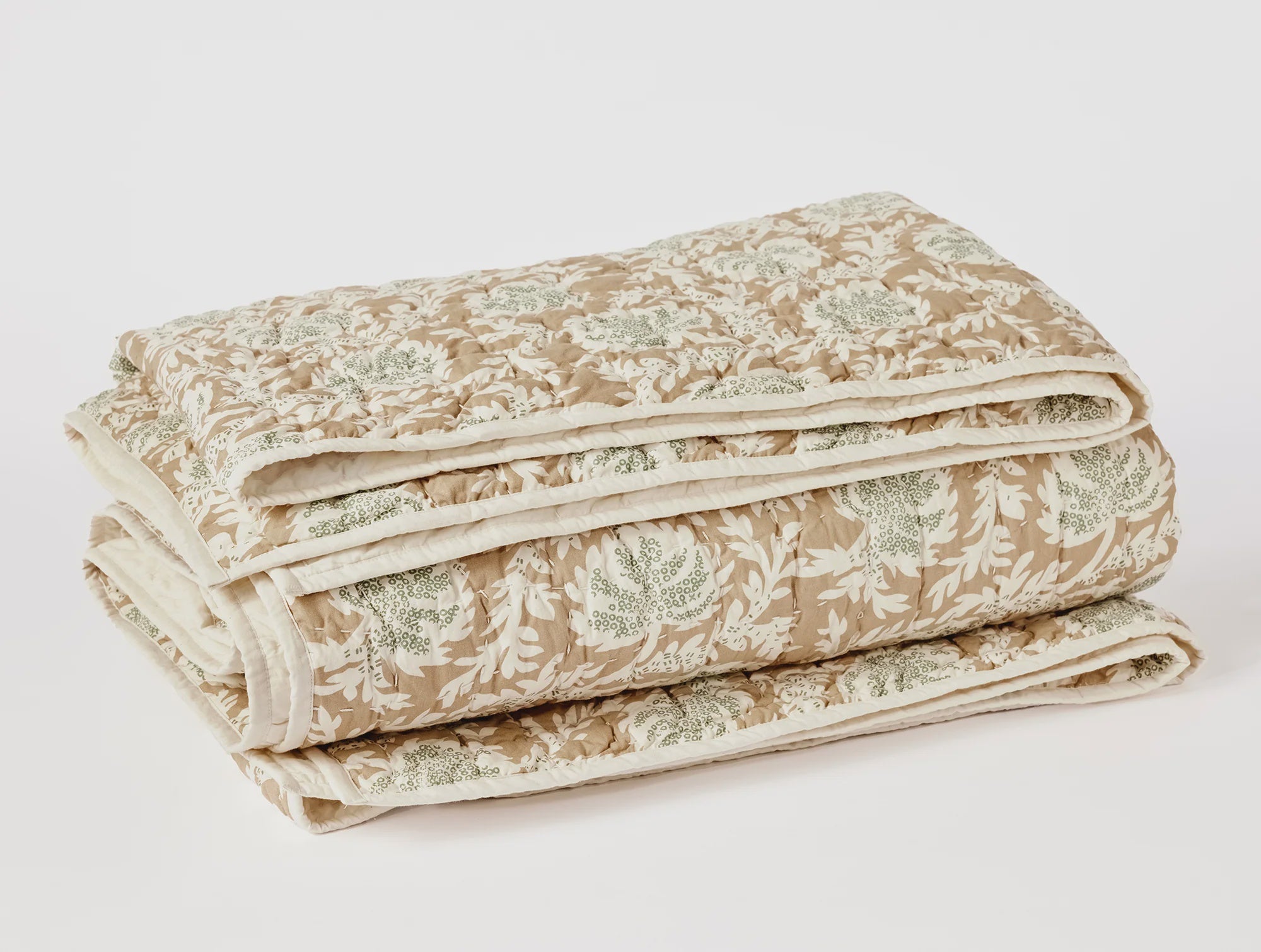 A folded Robles Handstitched Org Quilt with a floral pattern in shades of beige and green, neatly arranged against a plain white background, perfect for the cozy interior of a Scottsdale, Arizona bungalow by Coyuchi Inc.
