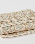 A folded Robles Handstitched Org Quilt with a floral pattern in shades of beige and green, neatly arranged against a plain white background, perfect for the cozy interior of a Scottsdale, Arizona bungalow by Coyuchi Inc.