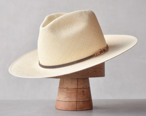A stylish, wide-brimmed Ninakuru Theo hat with a brown leather band, displayed on a wooden hat stand against a neutral gray background at a Scottsdale Arizona Bungalow.