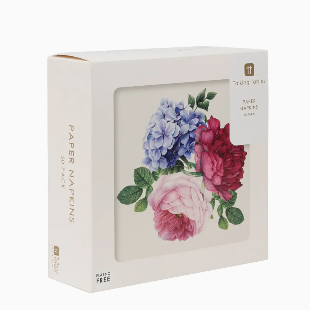 A package of Faire brand Floral Napkins 50Pk, labeled as plastic-free, designed in the style of a Scottsdale bungalow, displaying a floral design with blue hydrangeas and pink roses, visible through a front window cutout.