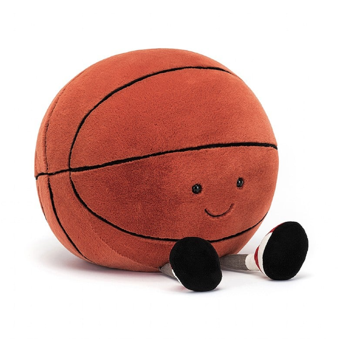 A plush toy designed to look like an Amuseable Basketball from Jelly Cat Inc., with arms and legs, sitting against a bungalow in Scottsdale, Arizona.