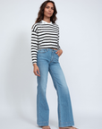 A person stands against a white background wearing an ASKK printed cropped long sleeve and wide-leg blue jeans. Barefoot with loose long hair, their effortless style embodies Los Angeles' laid-back vibe.