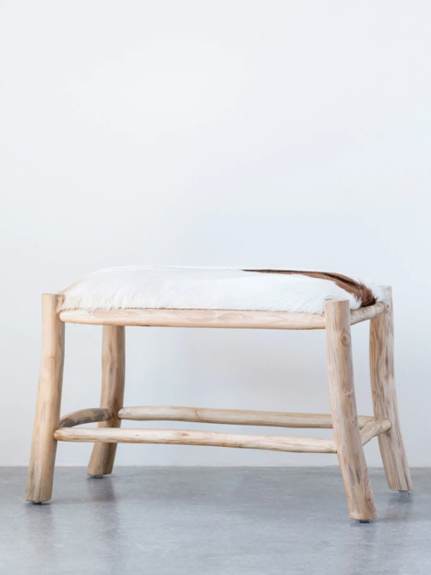 A minimalist Wood and Goat Hide Stool by Creative Co-op with a soft, white fur cushion on top, set against a plain gray background. The stool features a simple, rustic design influenced by Scottsdale Arizona aesthetics, with visible wood grains.