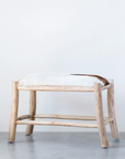 A minimalist Wood and Goat Hide Stool by Creative Co-op with a soft, white fur cushion on top, set against a plain gray background. The stool features a simple, rustic design influenced by Scottsdale Arizona aesthetics, with visible wood grains.