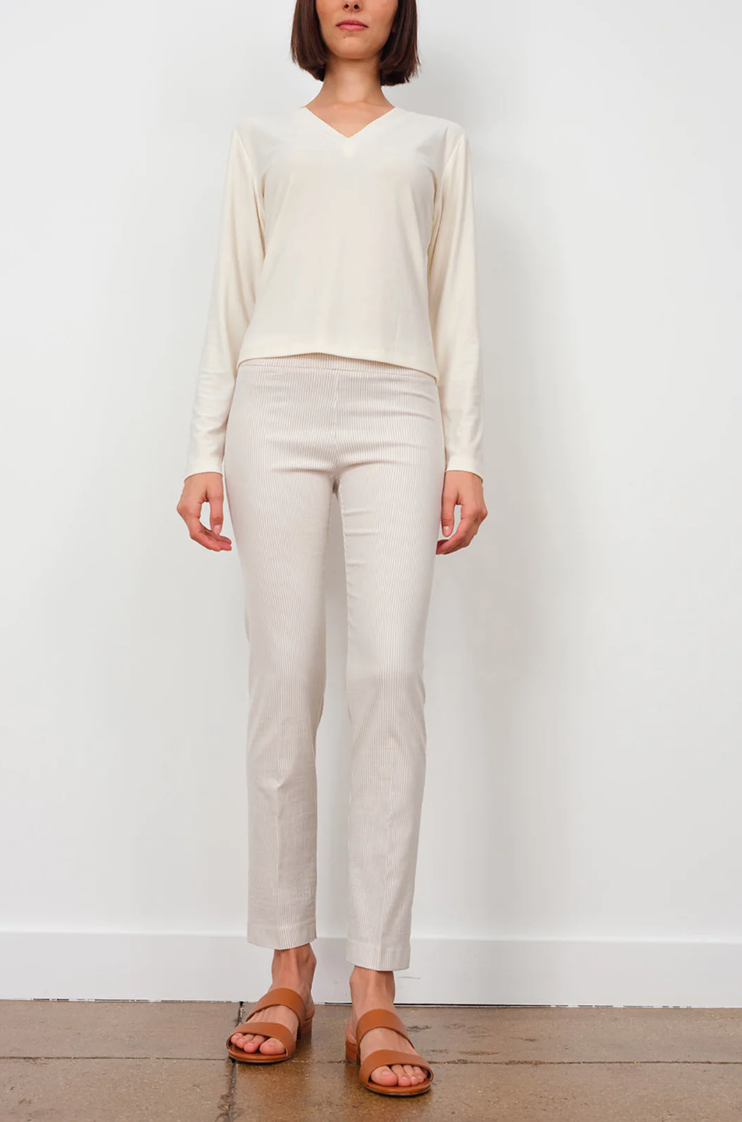 A woman stands against a plain background, wearing a cream V-neck blouse and matching Avenue Montaigne Lulu Pants with white sandals. Only the lower half of her face is visible, evoking the relaxed elegance of Scottsdale, Arizona.