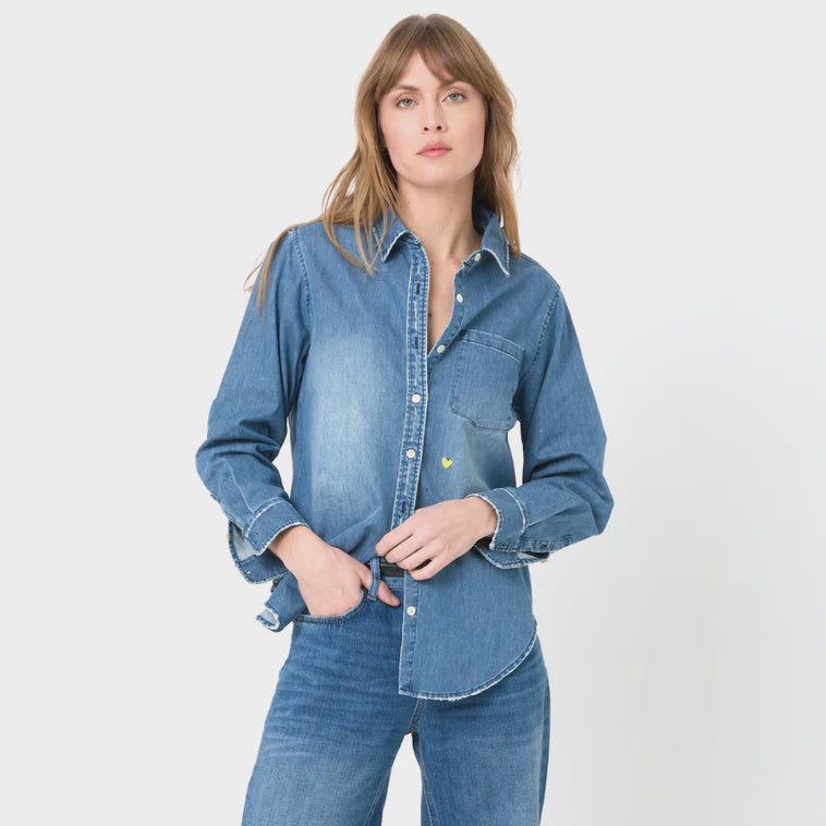 A woman in a stylish Mia Shirt Core True Denim by Kerri Rosenthal and jeans stands against a white background, looking directly at the camera with a slight smile. Her hands are casually placed on her waist, embodying an Arizona style.