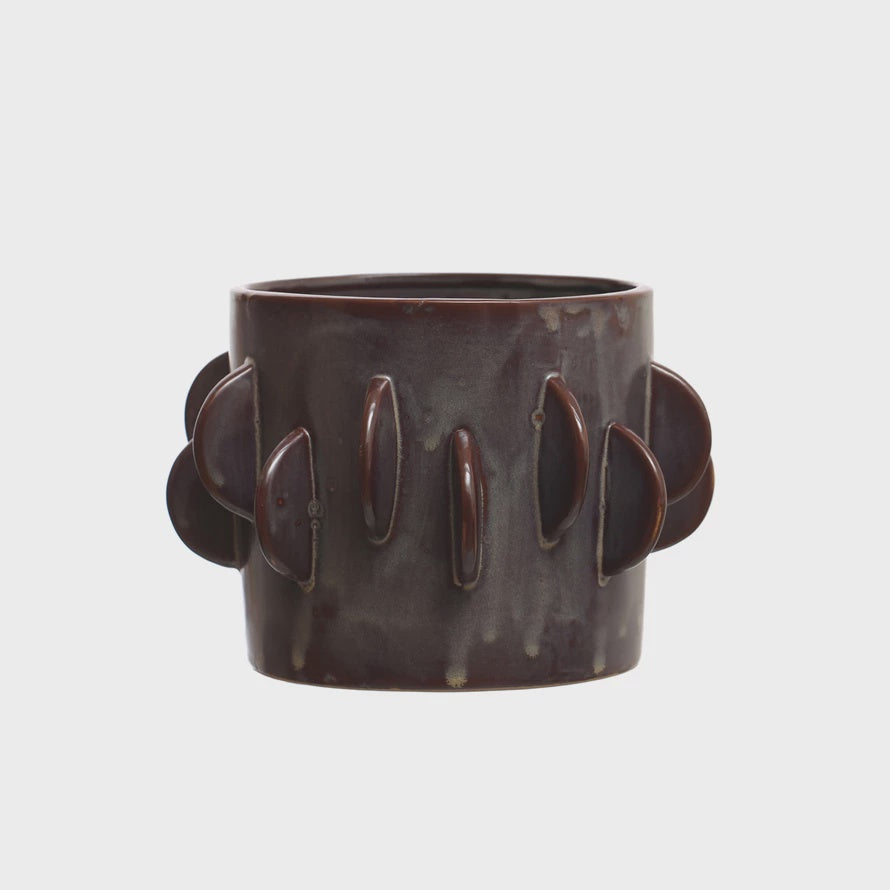 A cylindrical dark brown ceramic Bloomingville vase with multiple round, flat protrusions arranged symmetrically around its perimeter, isolated on a plain white background in a Scottsdale Arizona bungalow.