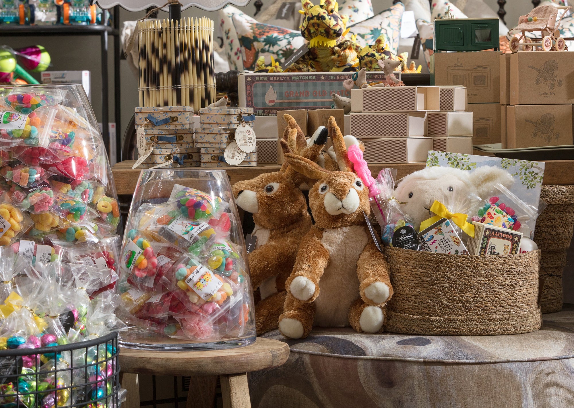 A store display with plush rabbits, baskets, and an assortment of candy in bags. Cardboard boxes and games are stacked on shelves. The scene is colorful and busy with various gift items.