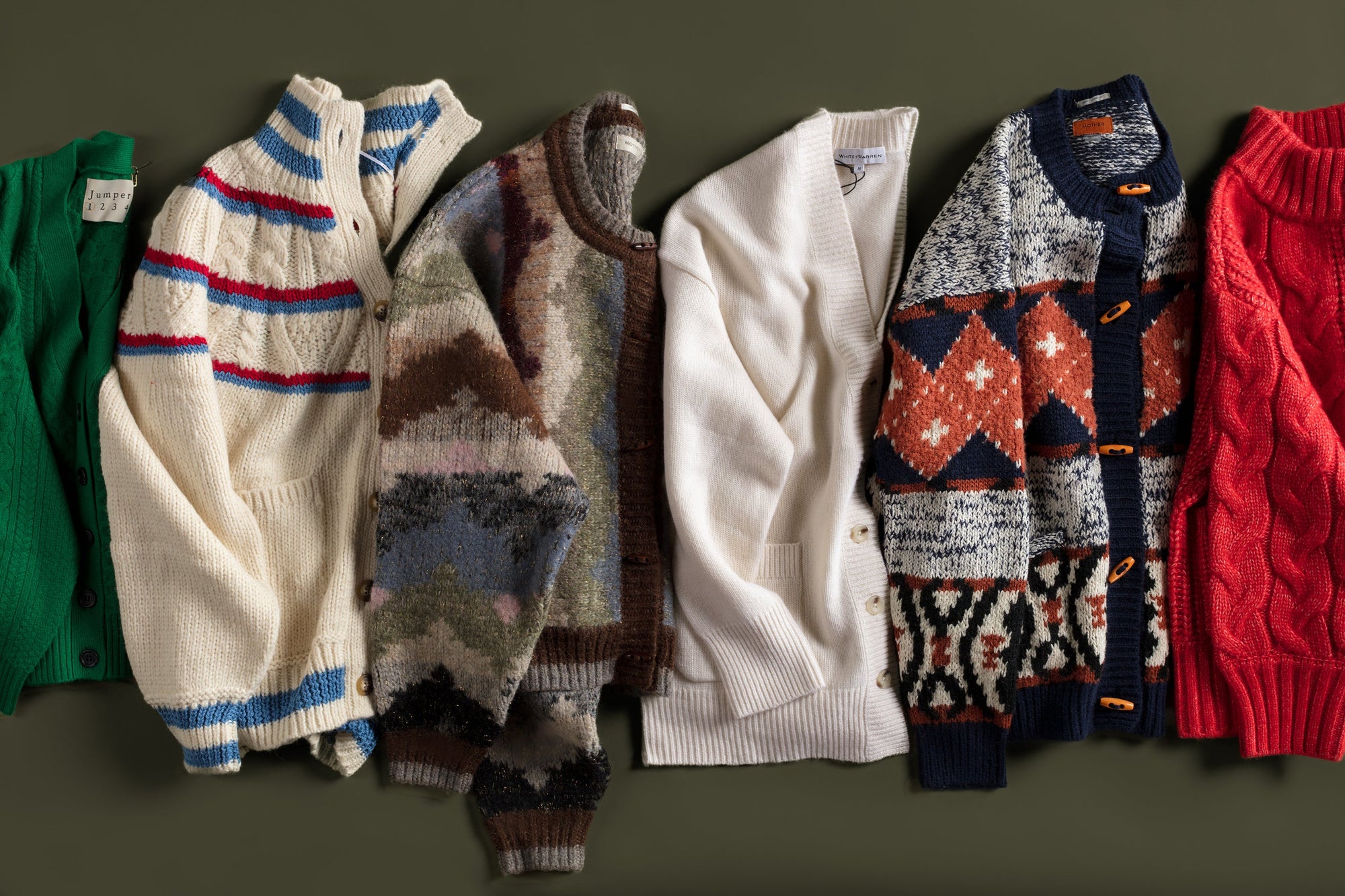 A row of seven cozy knit cardigans in various colors and patterns, including stripes, abstract designs, and solid colors, neatly arranged on a dark background.