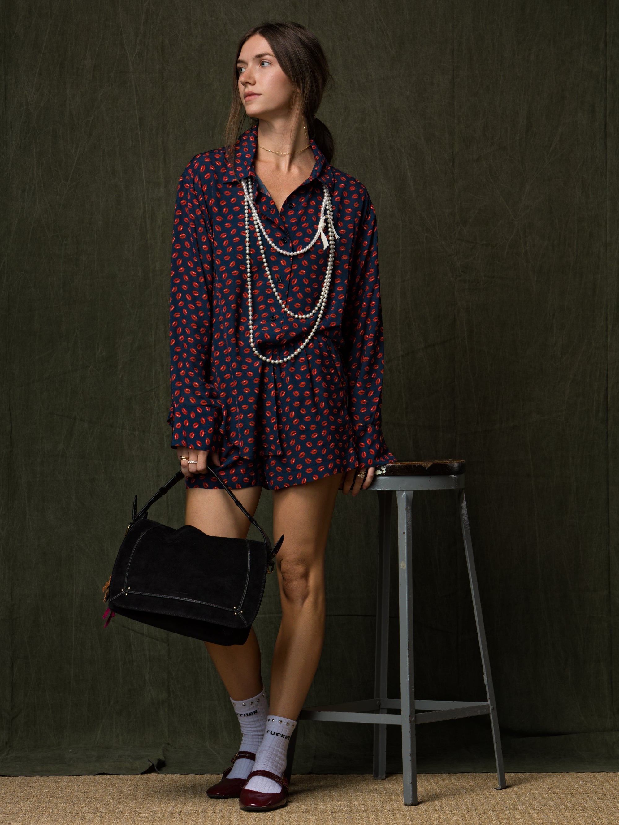 A woman in a leopard-print romper and brown sandals walks outdoors, holding a black textured handbag. She is near stone steps and greenery on a sunny day.