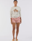 A person stands against a plain background wearing Le Superbe's Beaded Bananas Sweatshirt in ultra-soft fabric, paired with pink banana-patterned shorts and yellow flip-flops.