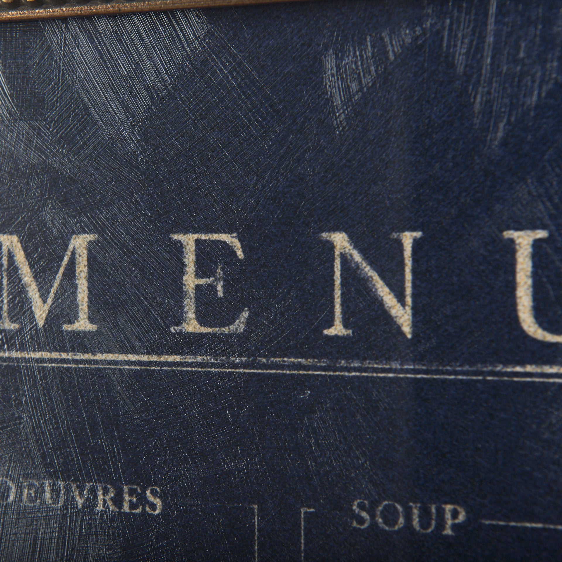 Close-up of a worn, textured Menu Art menu cover from a Scottsdale Arizona bungalow, with the word &quot;MENU&quot; embossed in gold lettering, showing signs of aging and scratches. Brand: Mercana