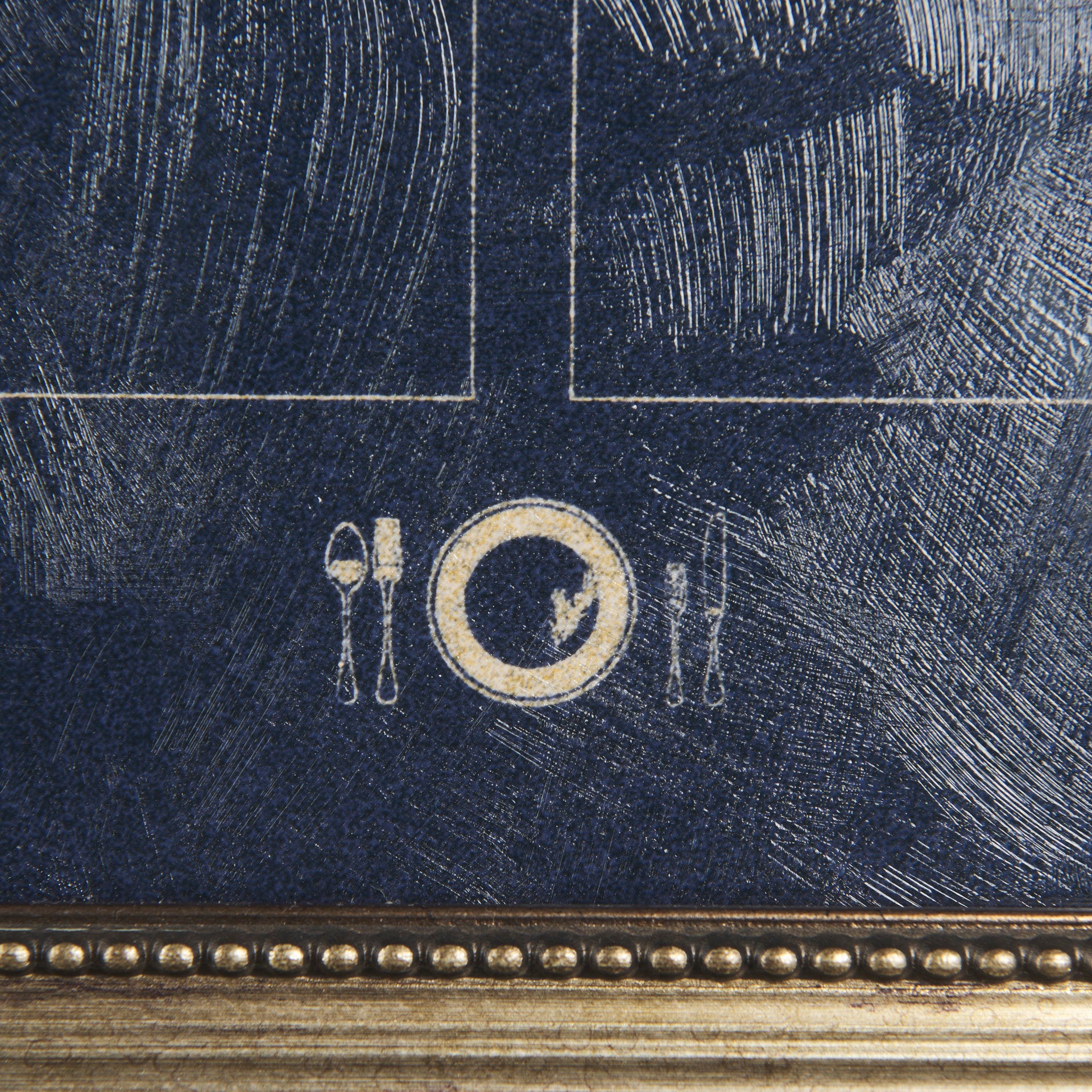 Close-up of a textured blue painting with marked white lines and a golden circular design featuring silhouette forks and a plate in the center, framed by an ornate golden border in a Mercana bungalow.
