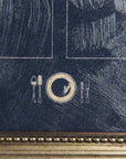 Close-up of a textured blue painting with marked white lines and a golden circular design featuring silhouette forks and a plate in the center, framed by an ornate golden border in a Mercana bungalow.