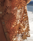 Close-up of Le Superbe's Suntan Camp Shirt, a sheer peach blouse with intricate floral lace, scalloped hem, and button details. Sunlight highlights its delicate patterns and casts soft shadows through the fabric.