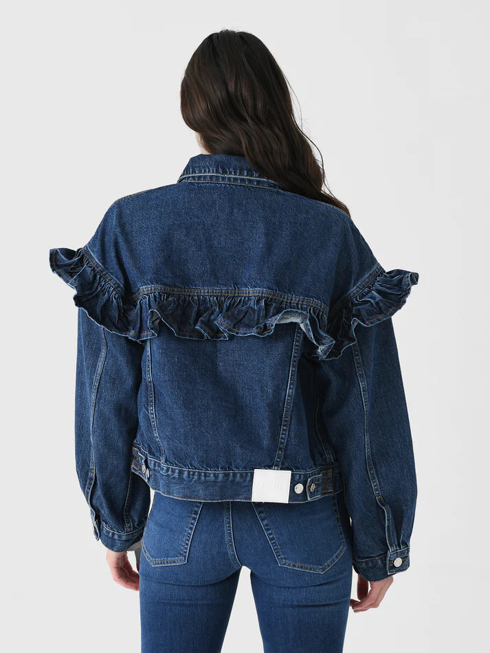 Rear view of a person wearing the FRAME Ruffle Jacket, featuring classic fit denim with ruffle detailing on the back and shoulders. The individual has long dark hair, styled with matching denim jeans for a cohesive look.