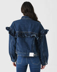 Rear view of a person wearing the FRAME Ruffle Jacket, featuring classic fit denim with ruffle detailing on the back and shoulders. The individual has long dark hair, styled with matching denim jeans for a cohesive look.