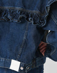 A close-up of FRAME's Ruffle Jacket with visible stitching, ruffle detail on back and sleeves, a white label at the bottom, held by a person in matching jeans.