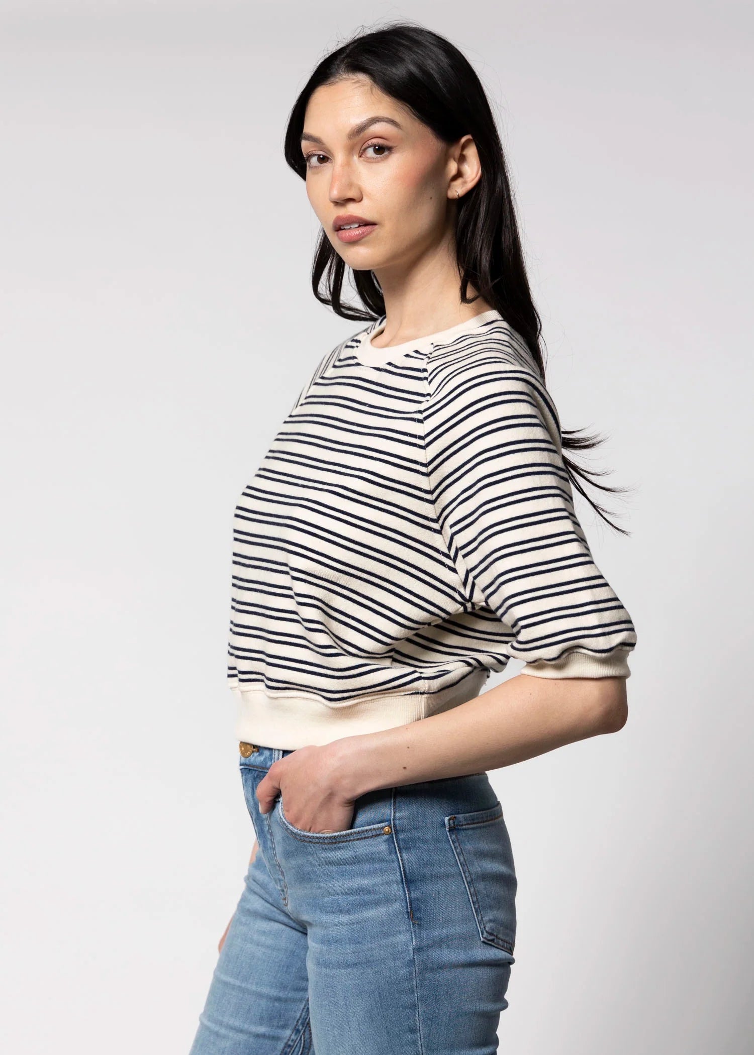 A woman with long dark hair models the Perfectwhitetee French Terry SS Raglan Sweatshirt with short sleeves, paired with blue jeans, posing in profile against a plain light background.