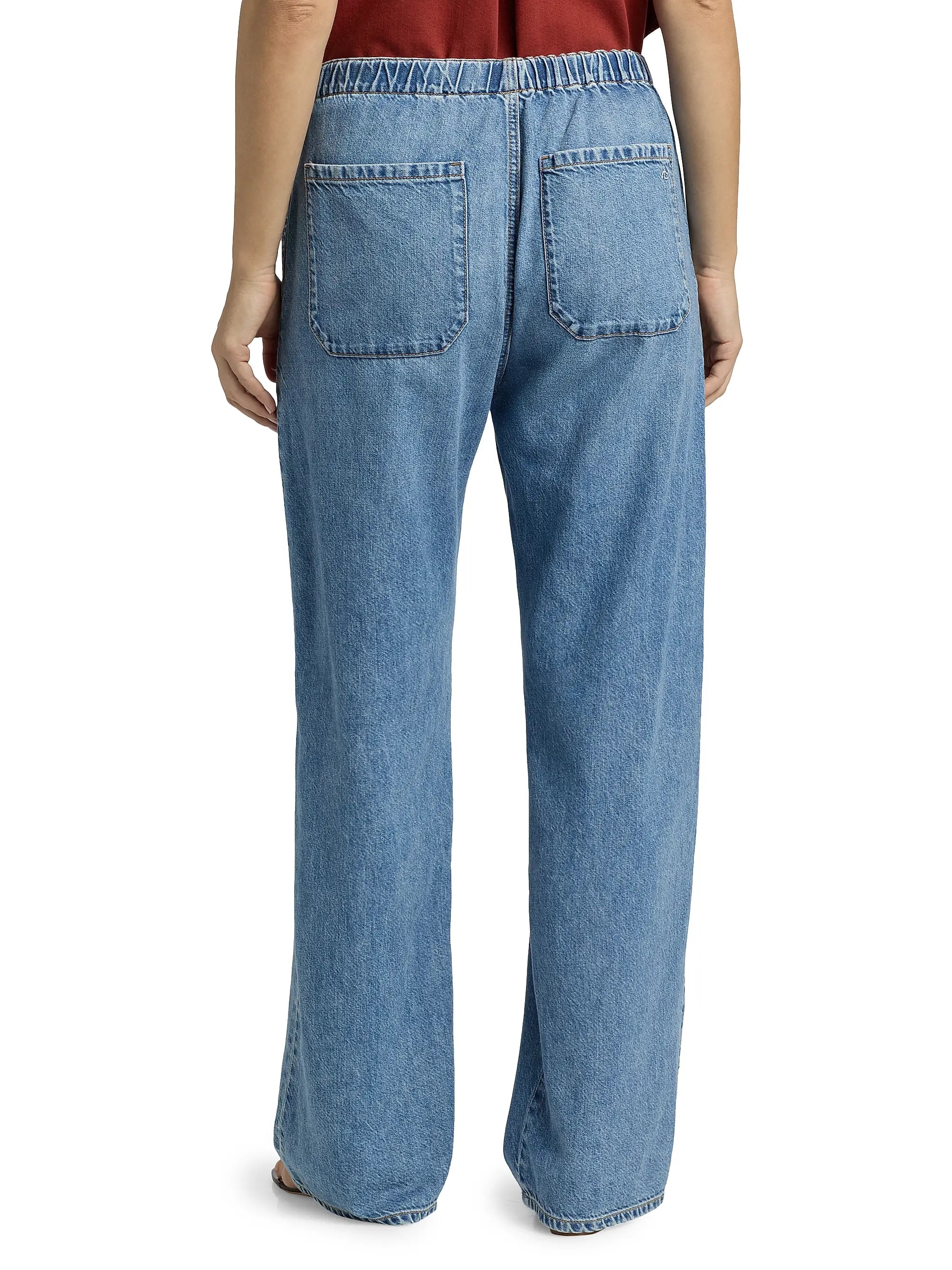 Someone stands with their back to the camera, wearing Rag & Bone ftwt logan pull on track jeans—relaxed straight fit in blue cotton-blend denim with an elastic waistband and two back pockets.