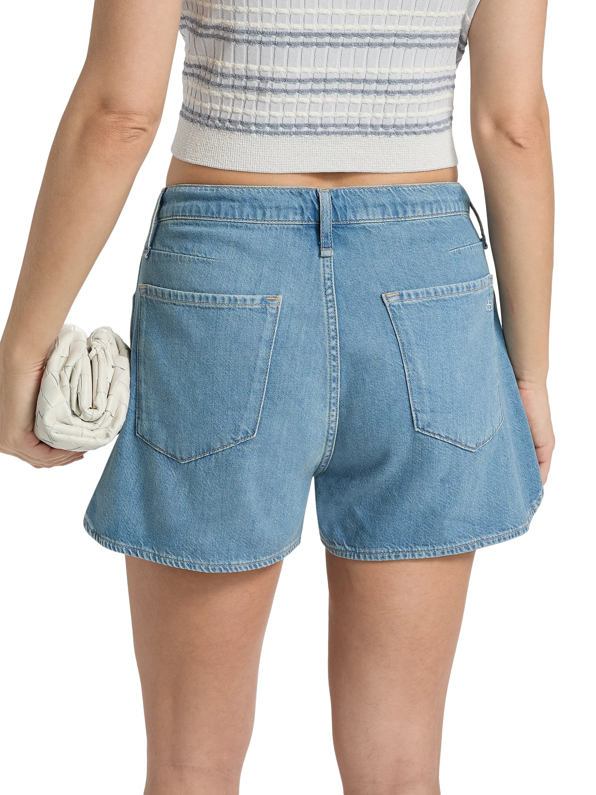 Wearing Rag &amp; Bone uftwt nolan short in light blue with a drawstring waist and a white sleeveless ribbed crop top, this person stands back to camera, holding a white woven clutch in their left hand.