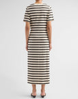 A person faces away, wearing Rag & Bone's the slub stripe tee midi dress—a short-sleeved, ankle-length cotton jersey with black, white, and beige stripes—paired with black heeled shoes for a classic look.