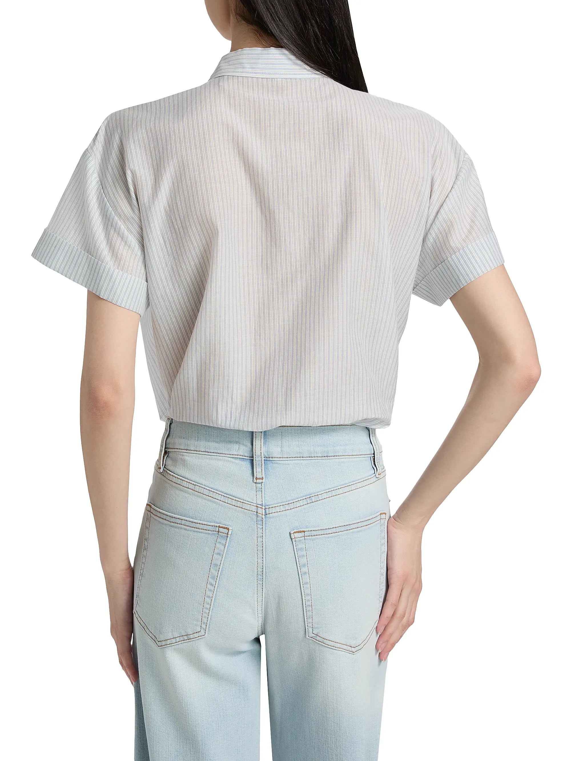 Someone is seen from behind wearing the light blue FRAME The Boardwalk Shirt with one hand on their hip, paired with light-wash jeans.