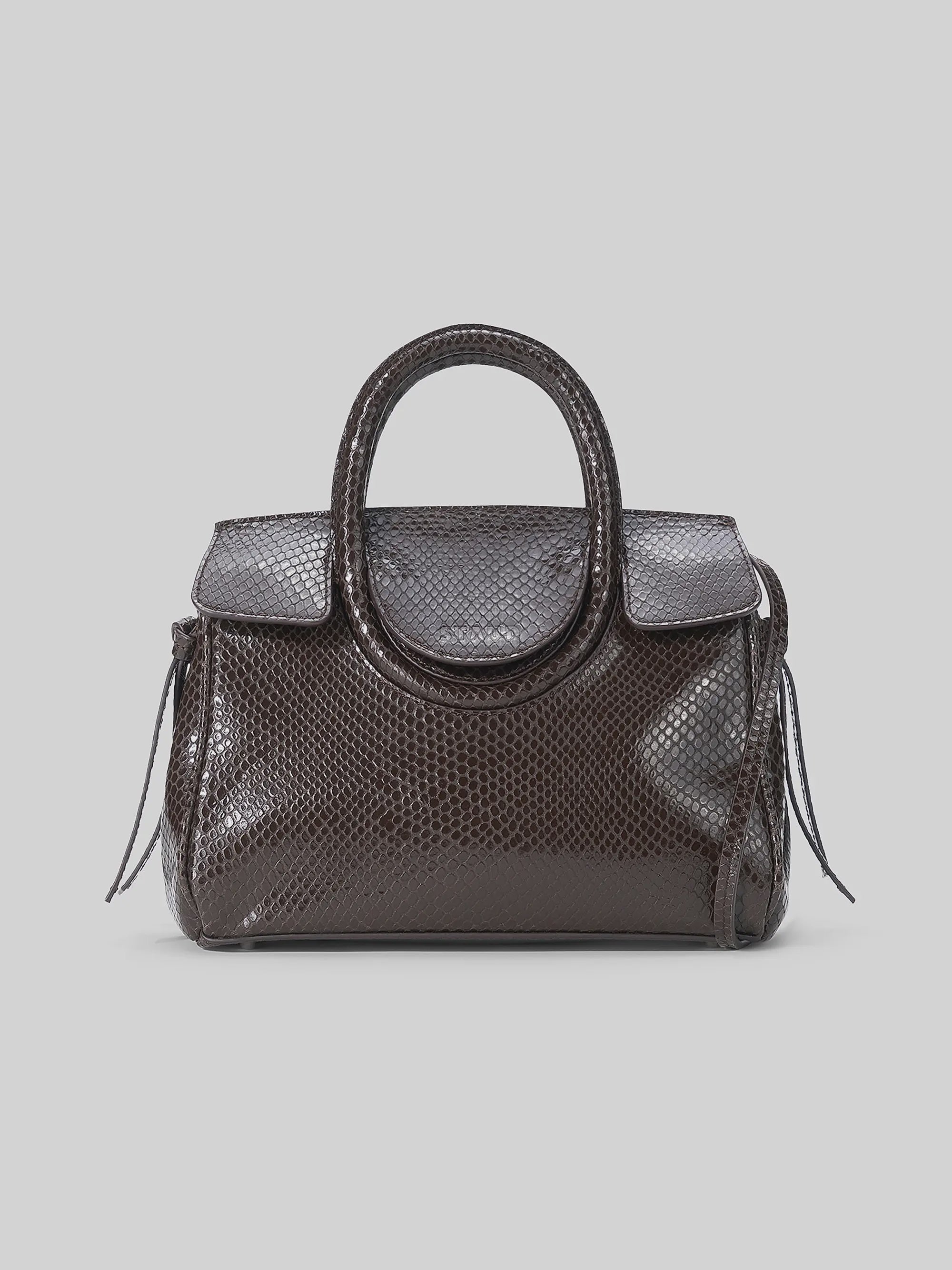 Dark brown snakeskin-embossed Staud Maude Mini Carryall with top handles and flap closure on light gray surface.
