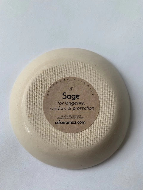 Turning over the Faire Ring Bowl reveals a label with "Sage for longevity, wisdom & protection," sharing its botanical symbolism and website, on a plain white background.