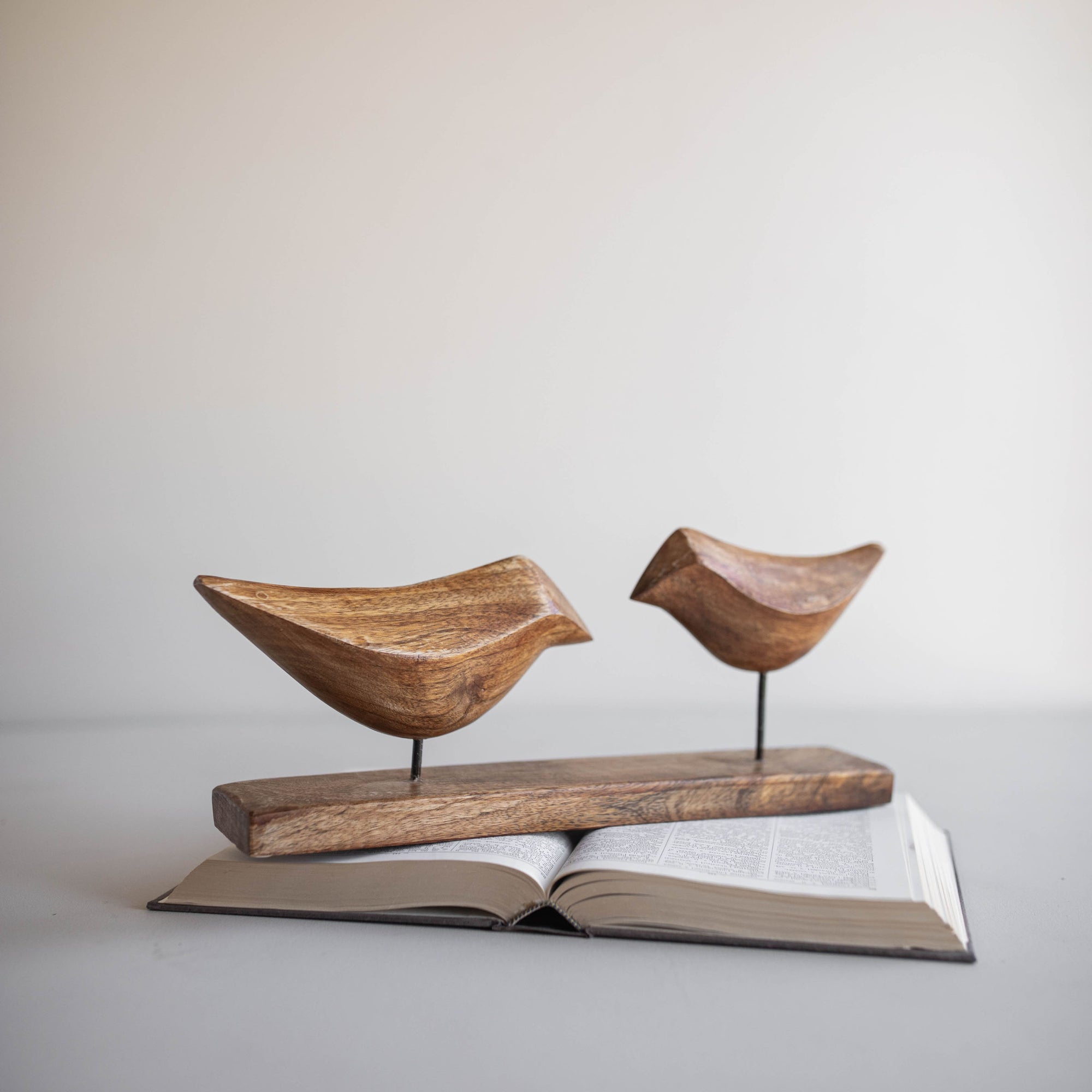 The Faire Arlo Natural Wood Decorative Birds feature two hand-carved mango wood birds on metal rods and a wooden base. Their simple design makes them an ideal accent for boho decor.