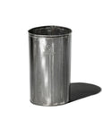 The Faire Steel Trashcan, a shiny cylindrical container made from recycled steel, stands upright on a white background. Its reflective surface casts a shadow to the right and displays a faint logo on the front.