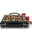 The Leopard Supreme Bag by Faire features a rectangular leopard print cowhide design, gold accents, a textured black bamboo handle, and a red bow with a gold tassel on the side, displayed against a white background.