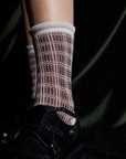 A close-up of feet in black leather shoes and Maria La Rosa Iceland Socks—women’s mid-calf merino wool with a red, black, and white plaid design—made in Italy, set against a dark background.