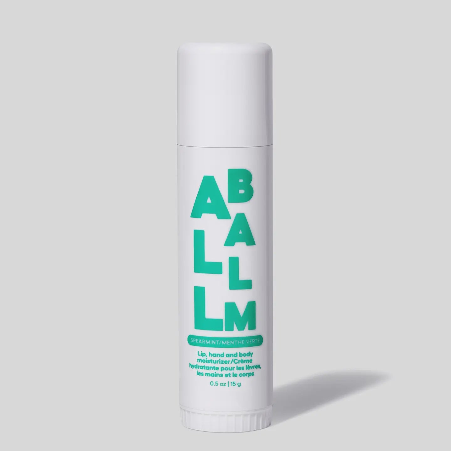 Against a gray background, a white tube of &quot;Faire All Balm Stick&quot; features bold green text: &quot;Spearmint Menthe Verte.&quot; This 0.5 oz/15 g balm provides non-greasy hydration for lips, hands, and body with natural ingredients.