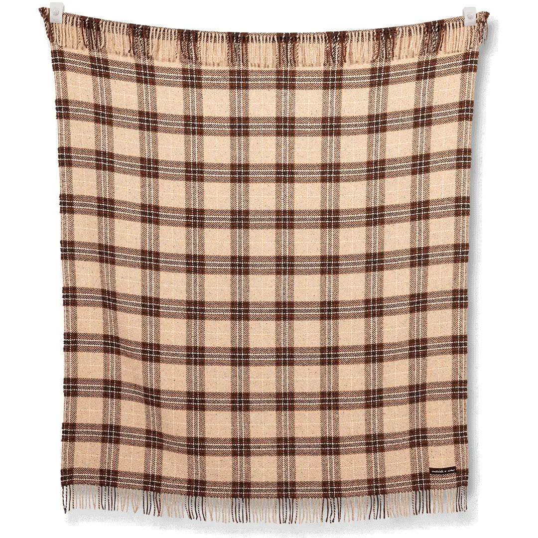 The S&A Blanket by Faire displays a vintage-inspired beige and brown plaid with a woven pattern, fringe edges, and a small fabric label in one corner, shown flat against a white background.