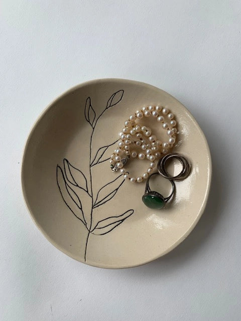 The Faire Ring Bowl, a hand-etched tray with botanical details, is perfect for holding pearl bracelets, beaded and green stone rings, and stacked silver rings—an ideal jewelry catch-all for any white surface.