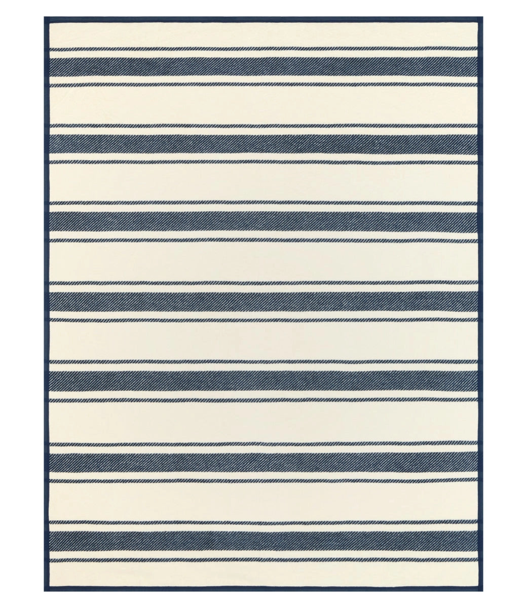 The Dockside Stripe Blanket by Faire features cream and navy blue stripes of varying thickness with a solid navy border, bringing a relaxed nautical style to any space.